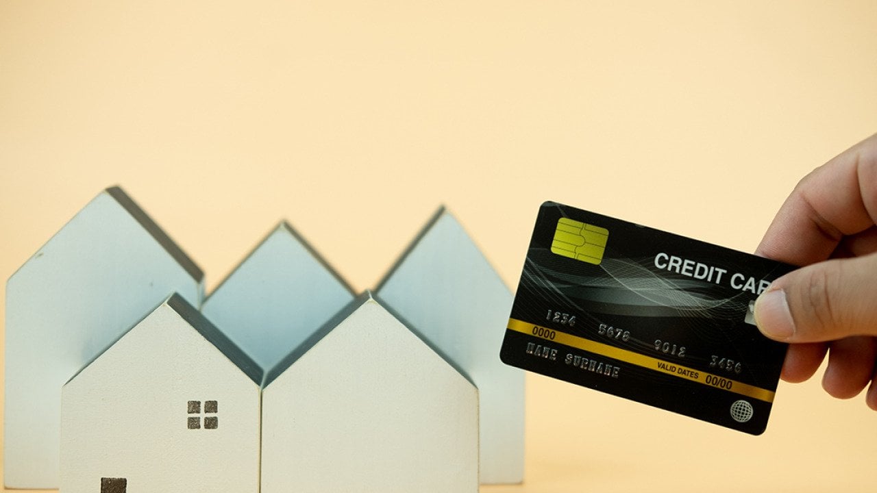 Hand holding a credit card over small figures of houses.