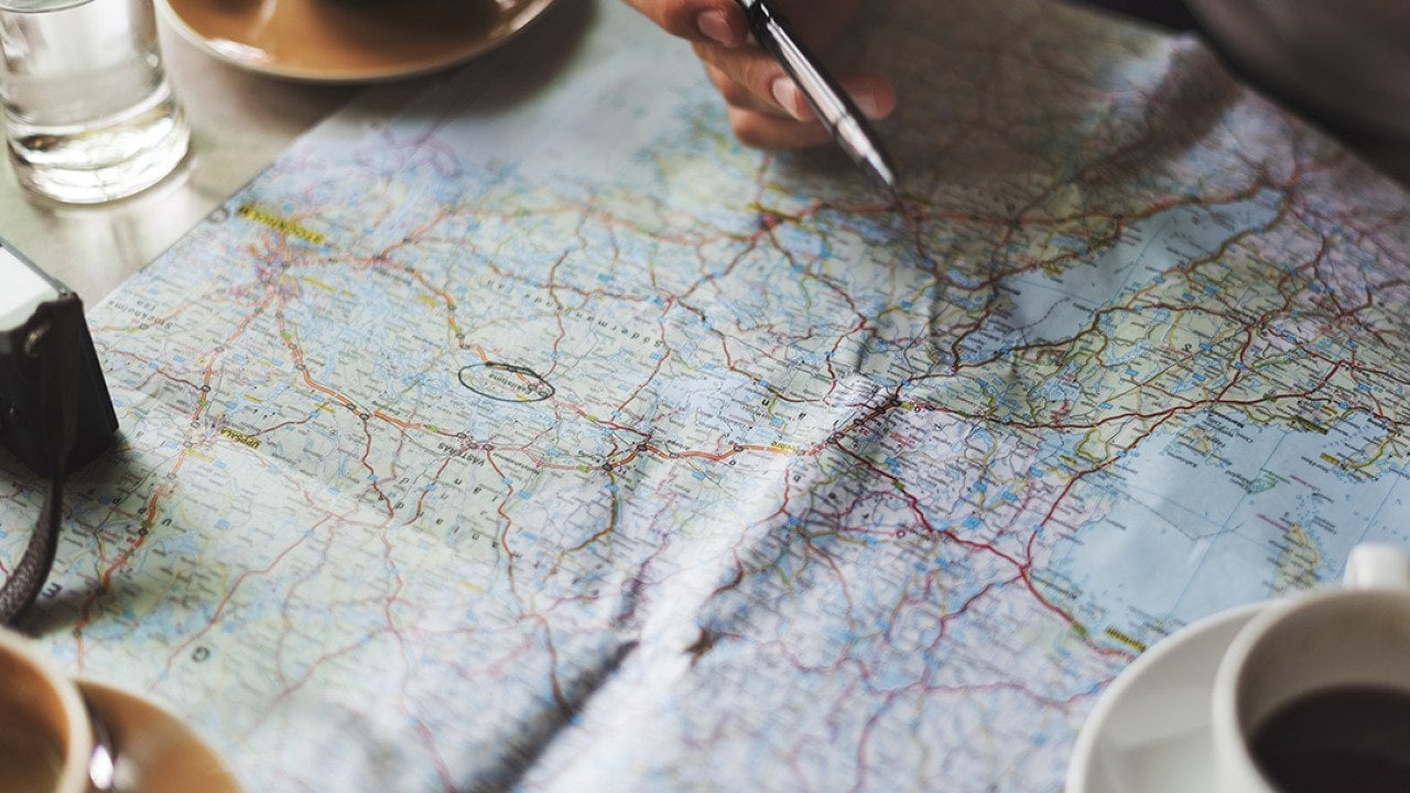 Person tracing a map with a pen for travel planning.