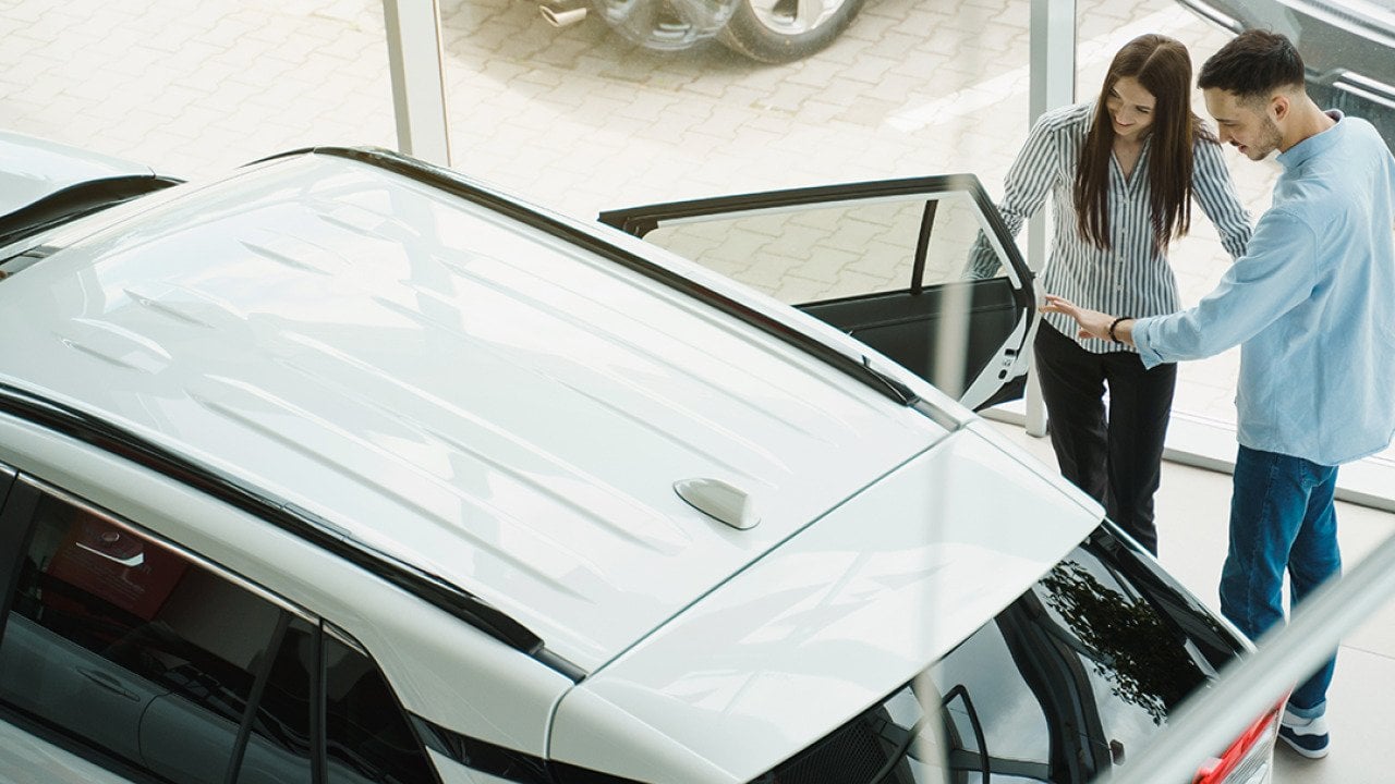 A young couple checking out a car at a dealership.