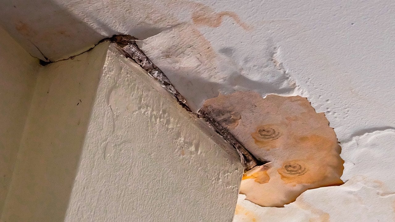 A corner of a home's ceiling falling apart from mold and water damage.