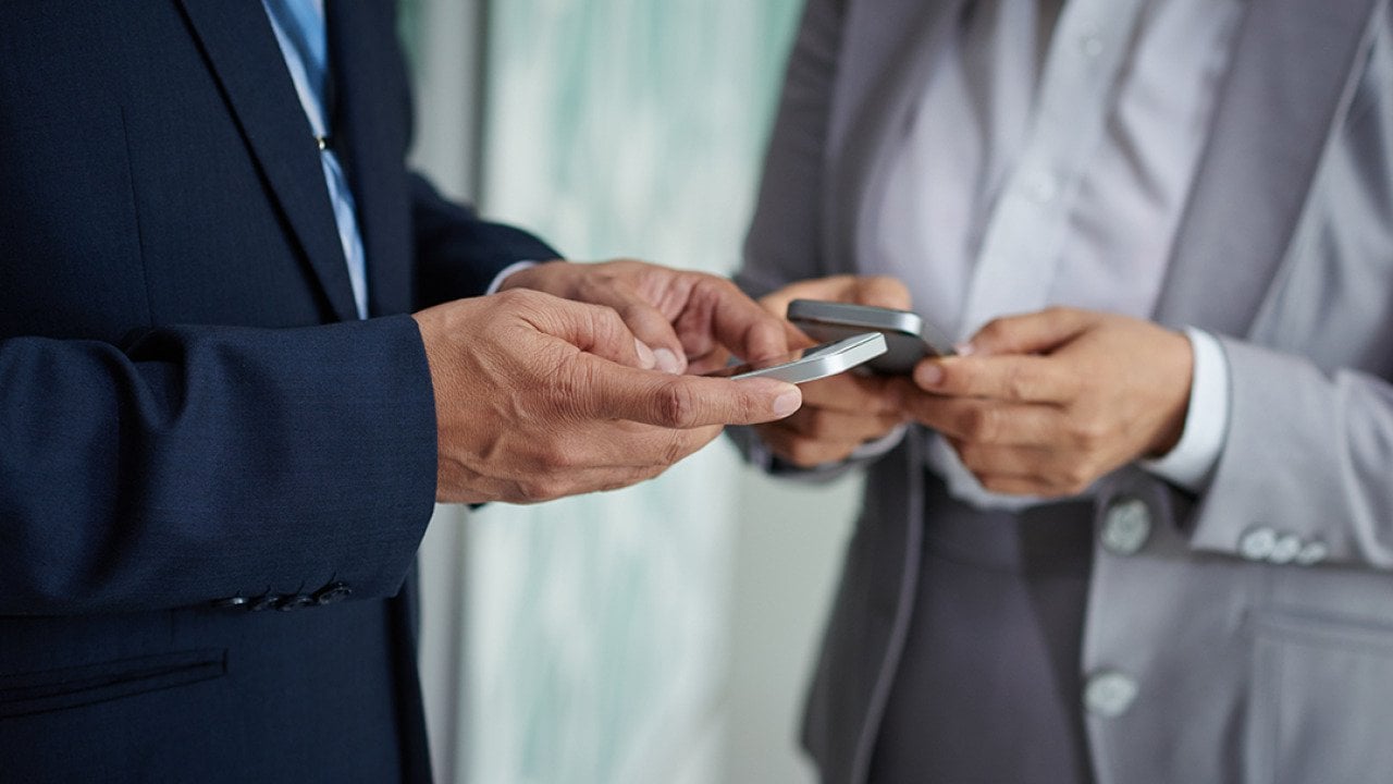 Two businesspeople on their phones exchanging numbers.