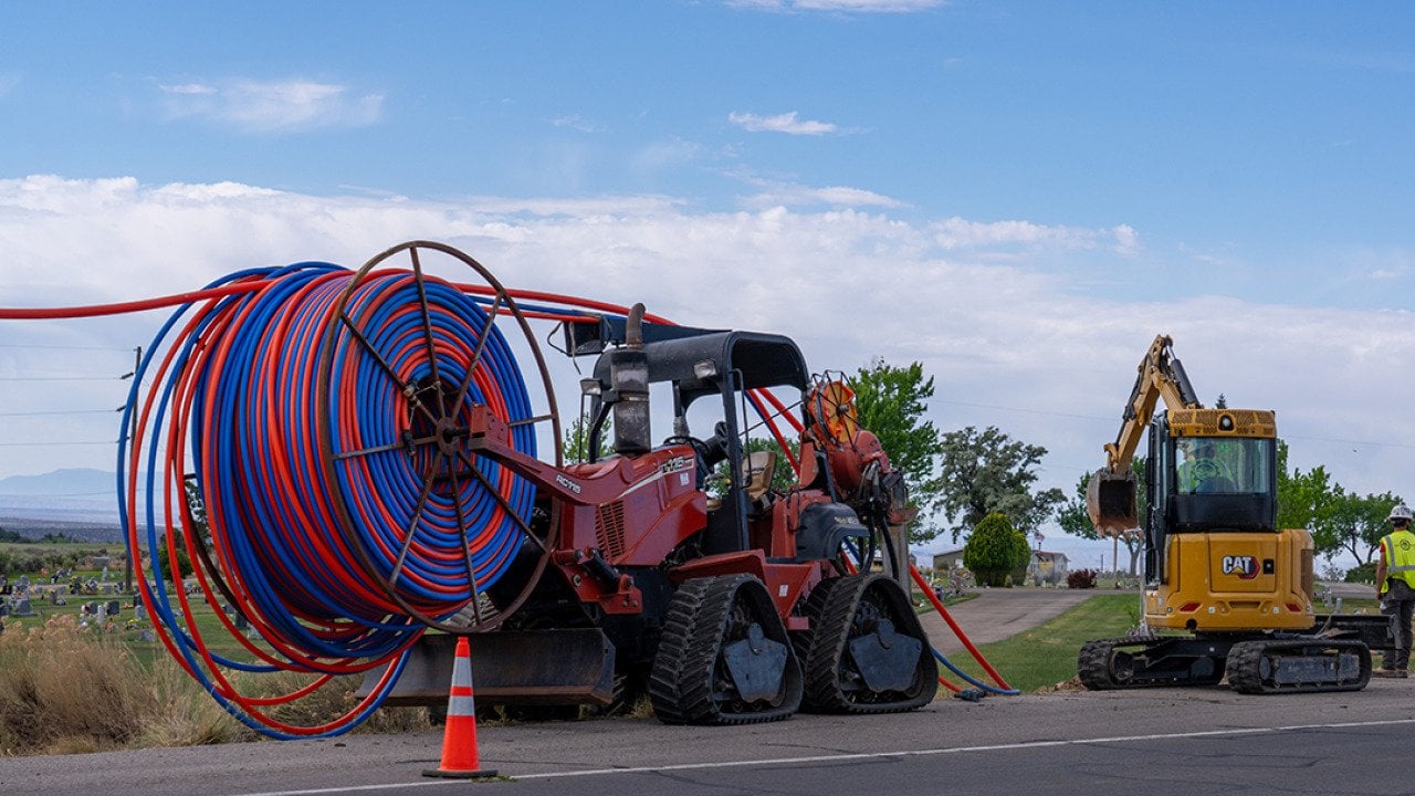 Machinery vehicles parked on roadside while installing internet fiber optic cables' plastic conduit underground in a rural area in Utah.