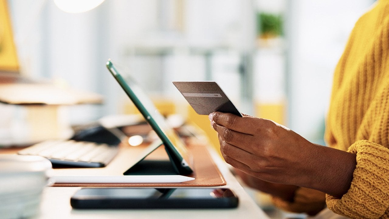 A businesswoman holding up a credit card while at work in the office.