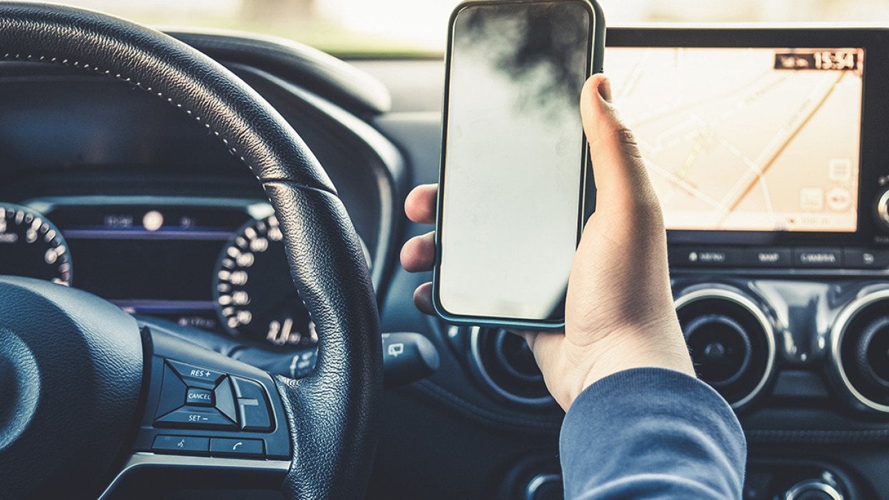 Person's hand holding up a smartphone while driving.
