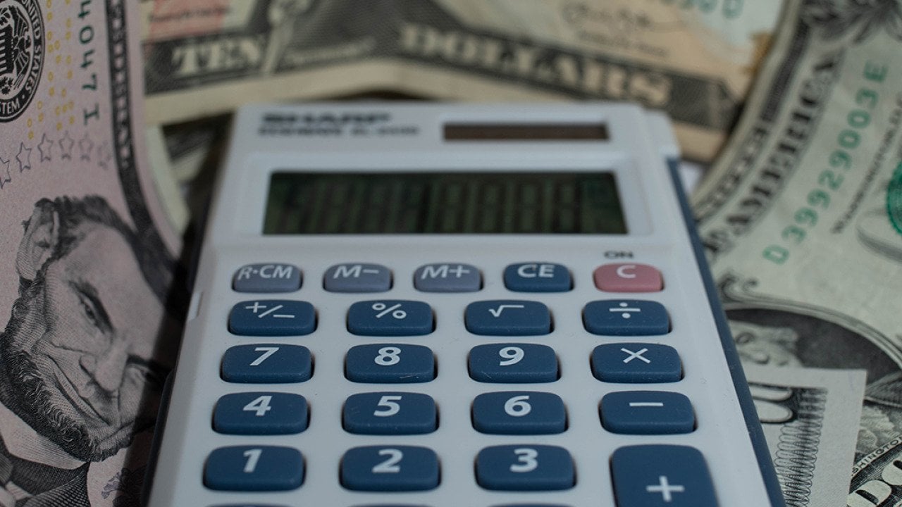 A calculator with a background of US dollar banknotes.