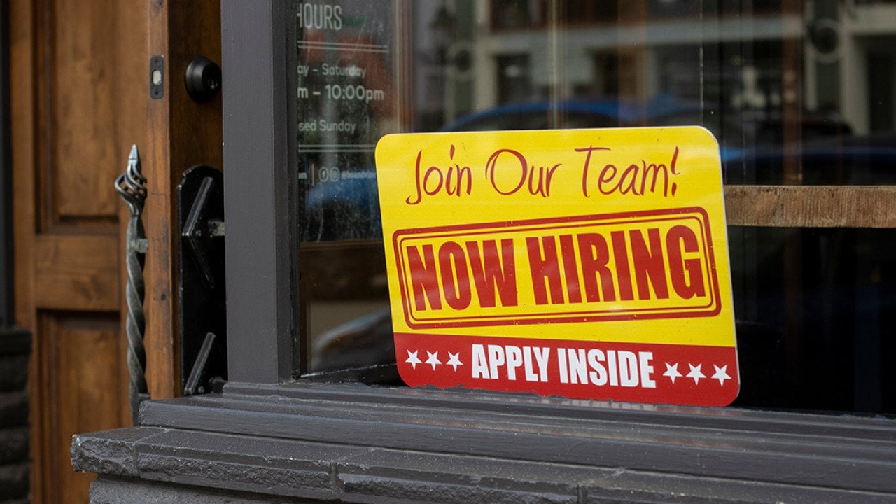 A 'now hiring' sign displayed on a glass window.
