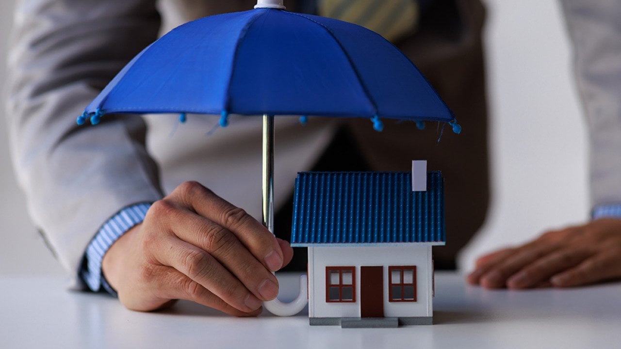 A figure of a house with a person holding small umbrella over it as a concept of home insurance.