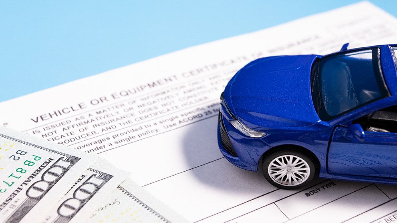 A small figure of a blue car on top of banknotes and insurance documents.