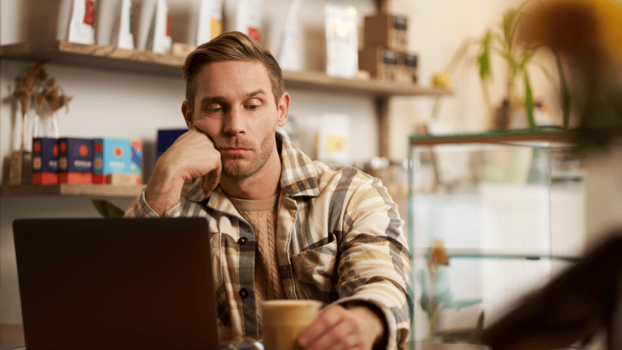 Man glumly staring at his laptop in a coffee shop.