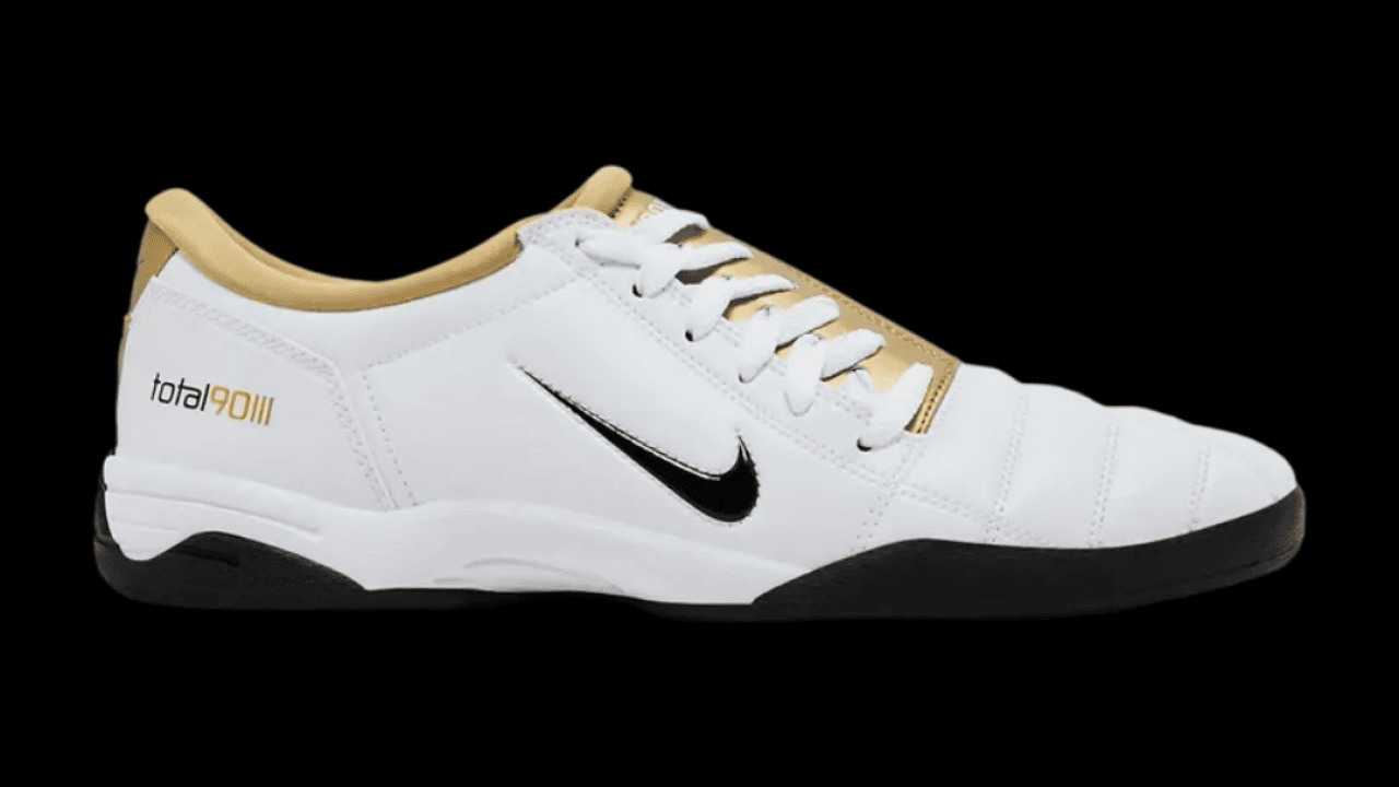 A pair of mostly white soccer shoes with a black Nike swoosh and a gold lining.
