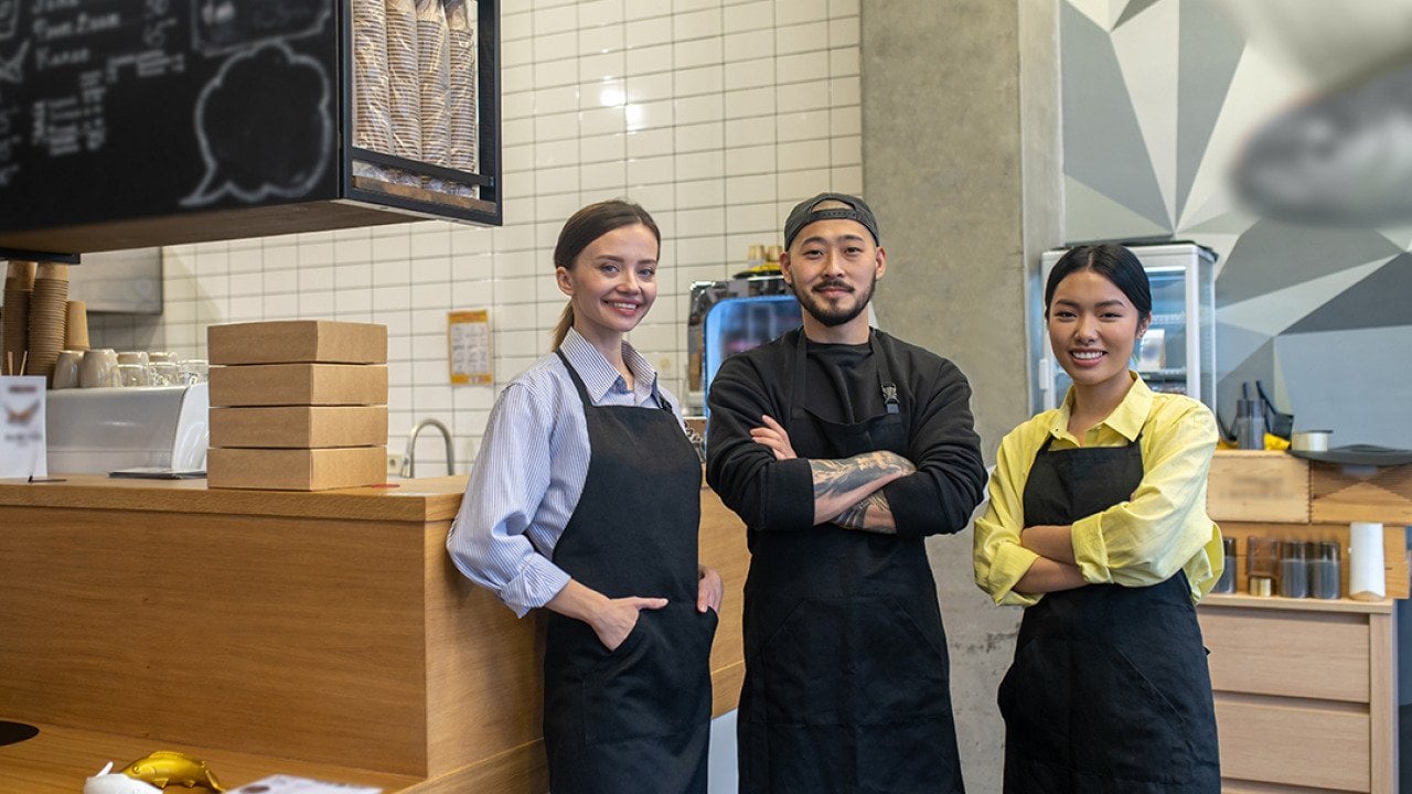 A team of young cafe workers pose in front of their shop's front bar.