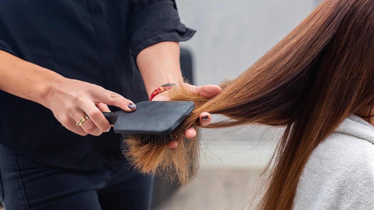 A professional hairstylist combing a client's hair with a paddle hairbrush.