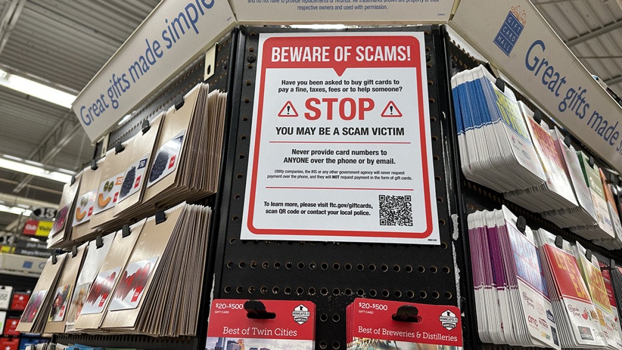 A large 'beware of scams' sign on display at a gift card aisle in a store.