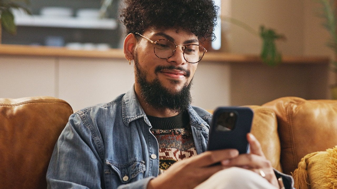 A young man smiling while typing on a smartphone.