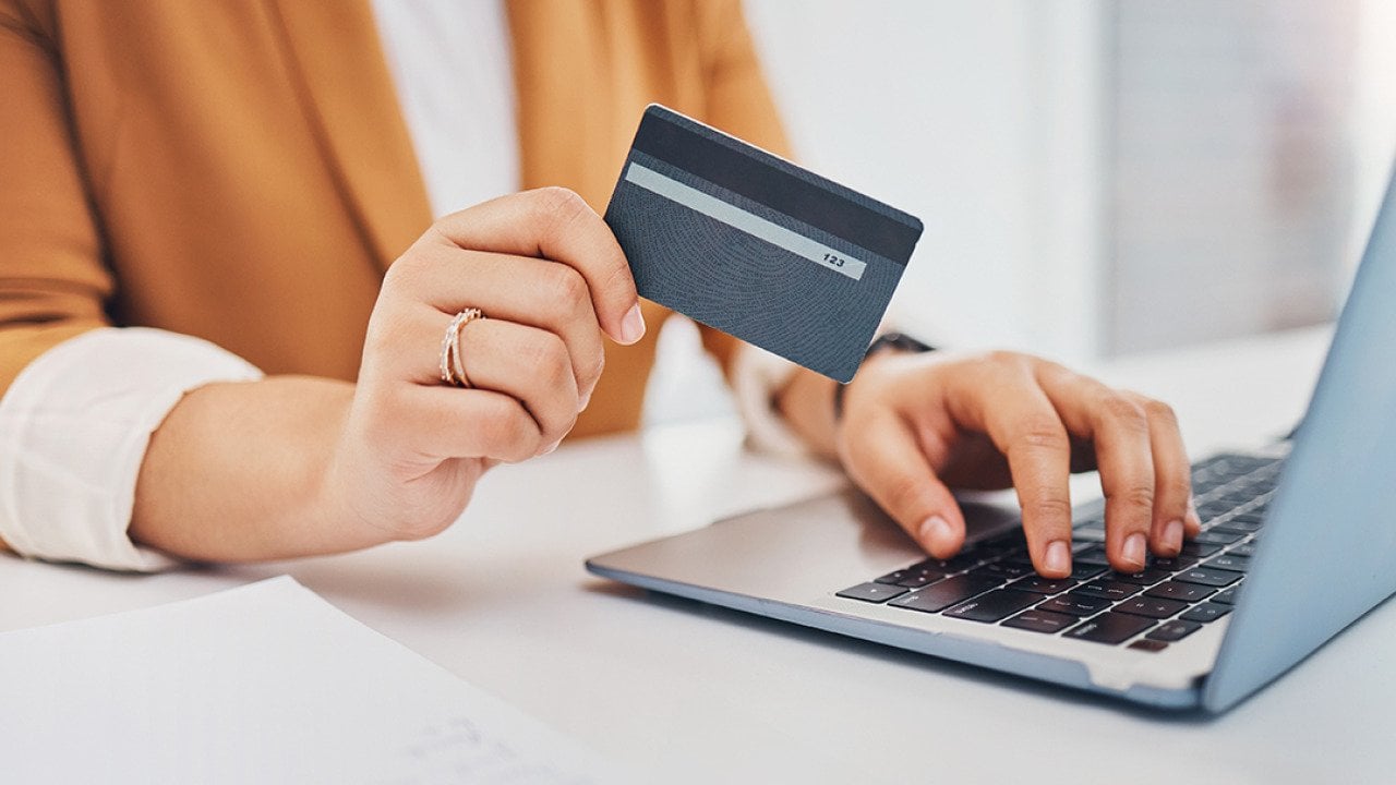 Person holding a credit card while using a laptop.