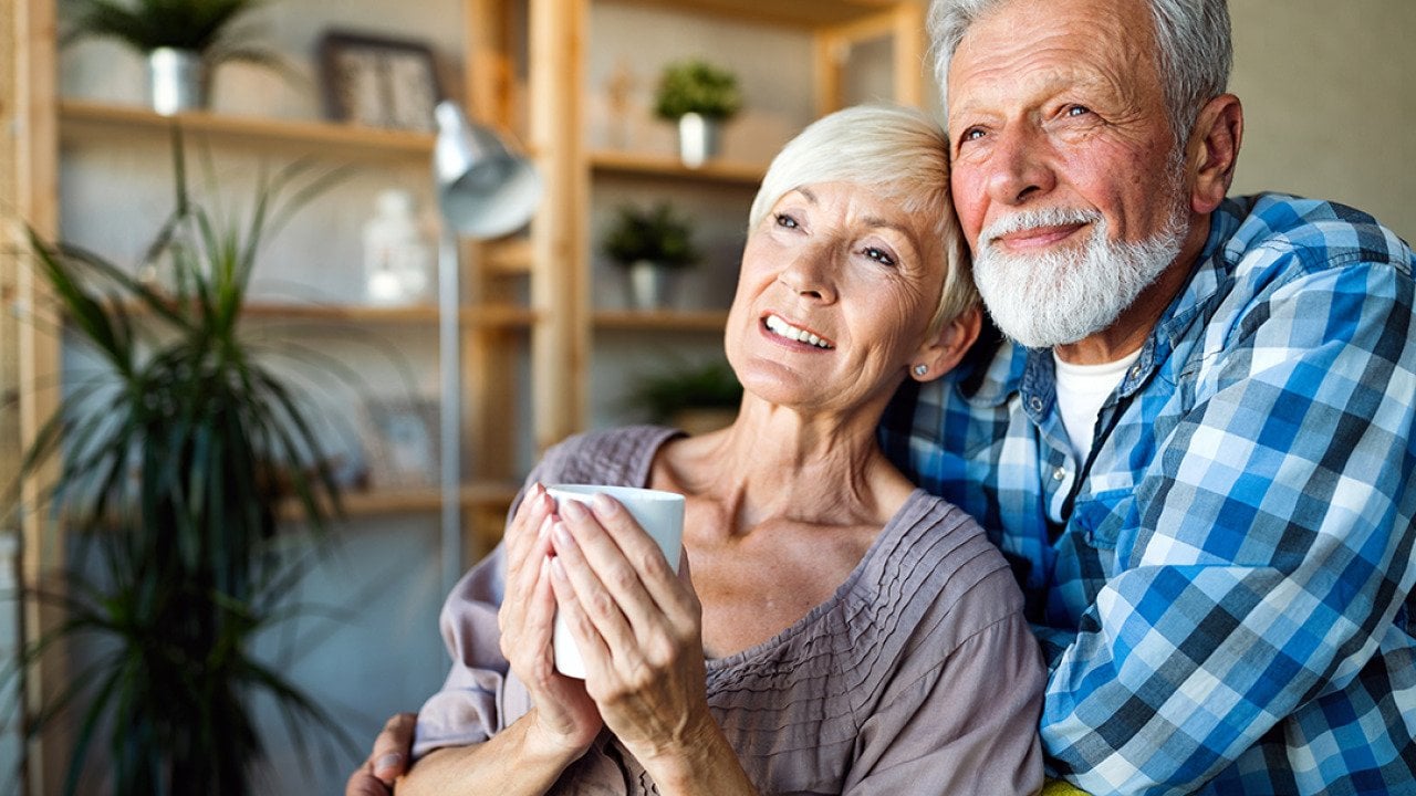 A senior couple hugging and looking out while having a coffee in the morning.