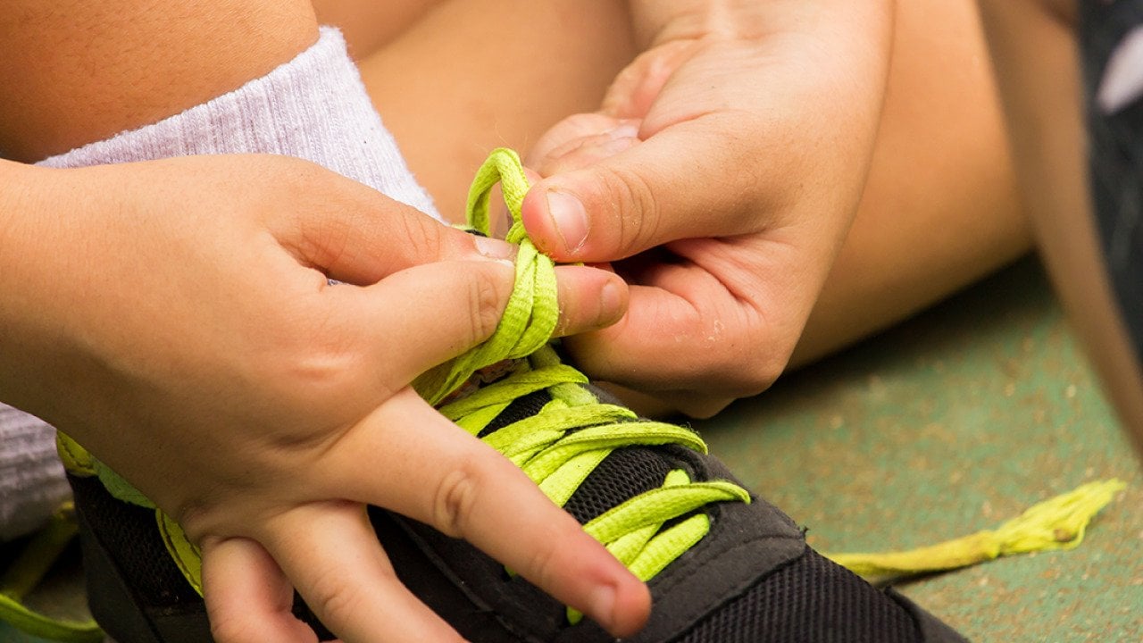 A young boy's hands tying shoelaces by himself.