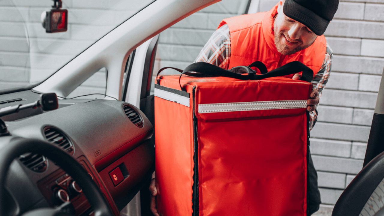A food delivery person putting zipping up his delivery bag in his car.