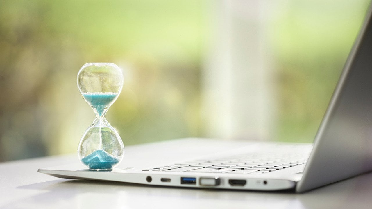 A small hourglass on top of a laptop as a concept of deadline and time management.
