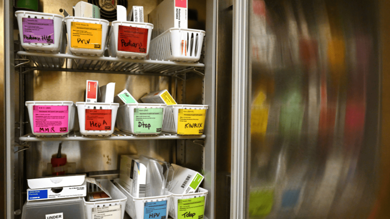 A small open refrigerator with shelves of baskets of vaccines at a health clinic.