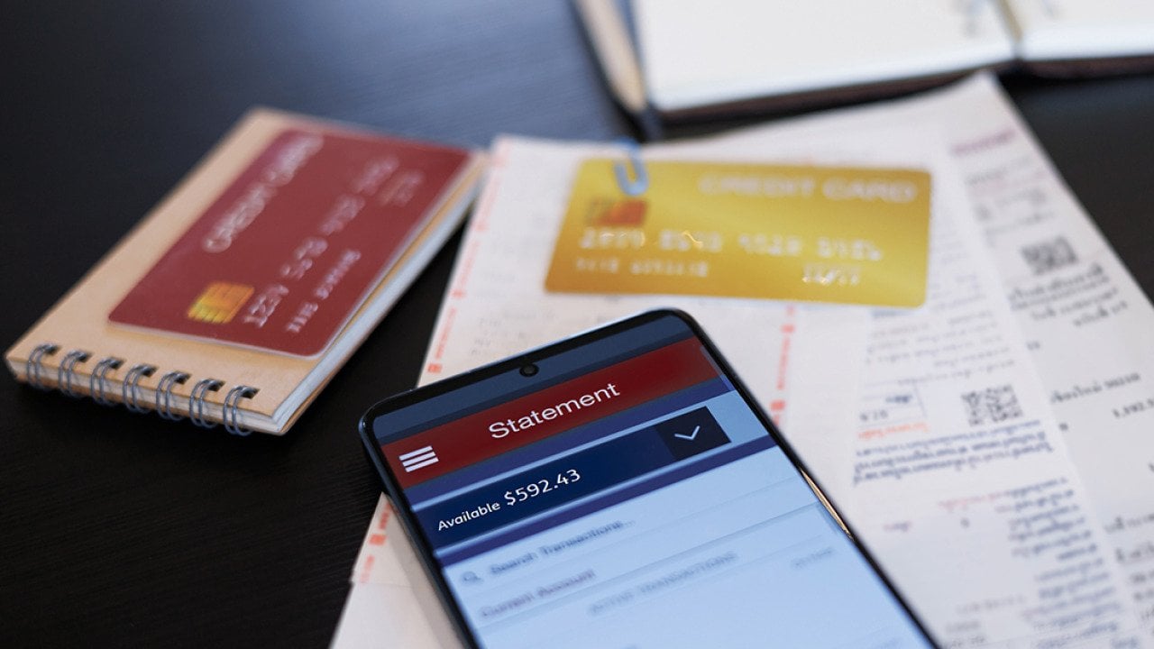 A close up on a credit card statement opened from a phone on top of physical credit cards and receipts.