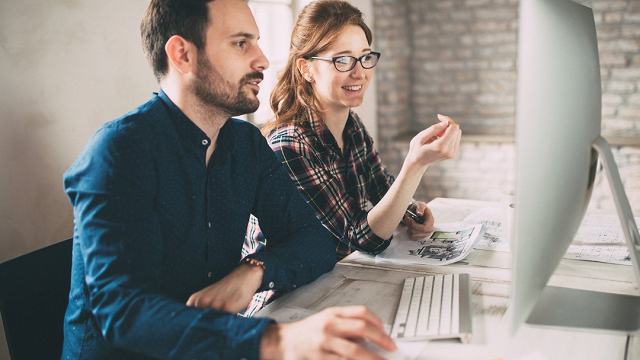 Two colleagues working in front of a computer monitor in an office.
