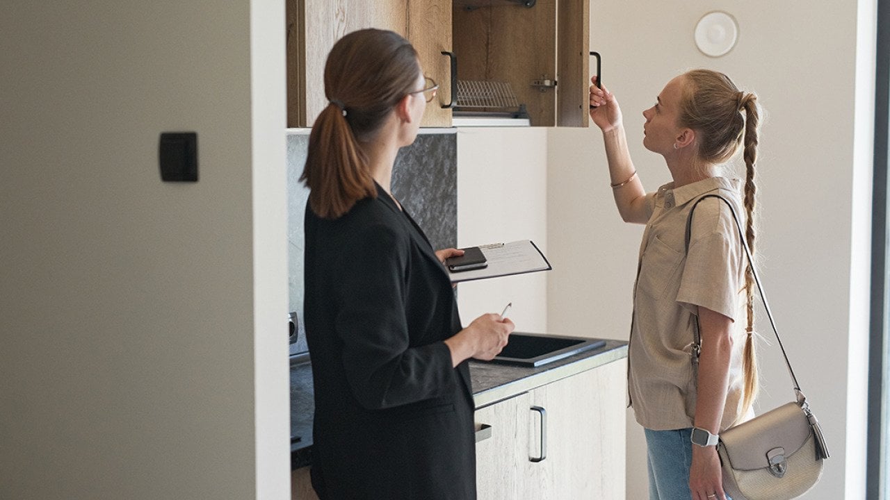 A young woman checking cabinets of an apartment with a female real estate agent.