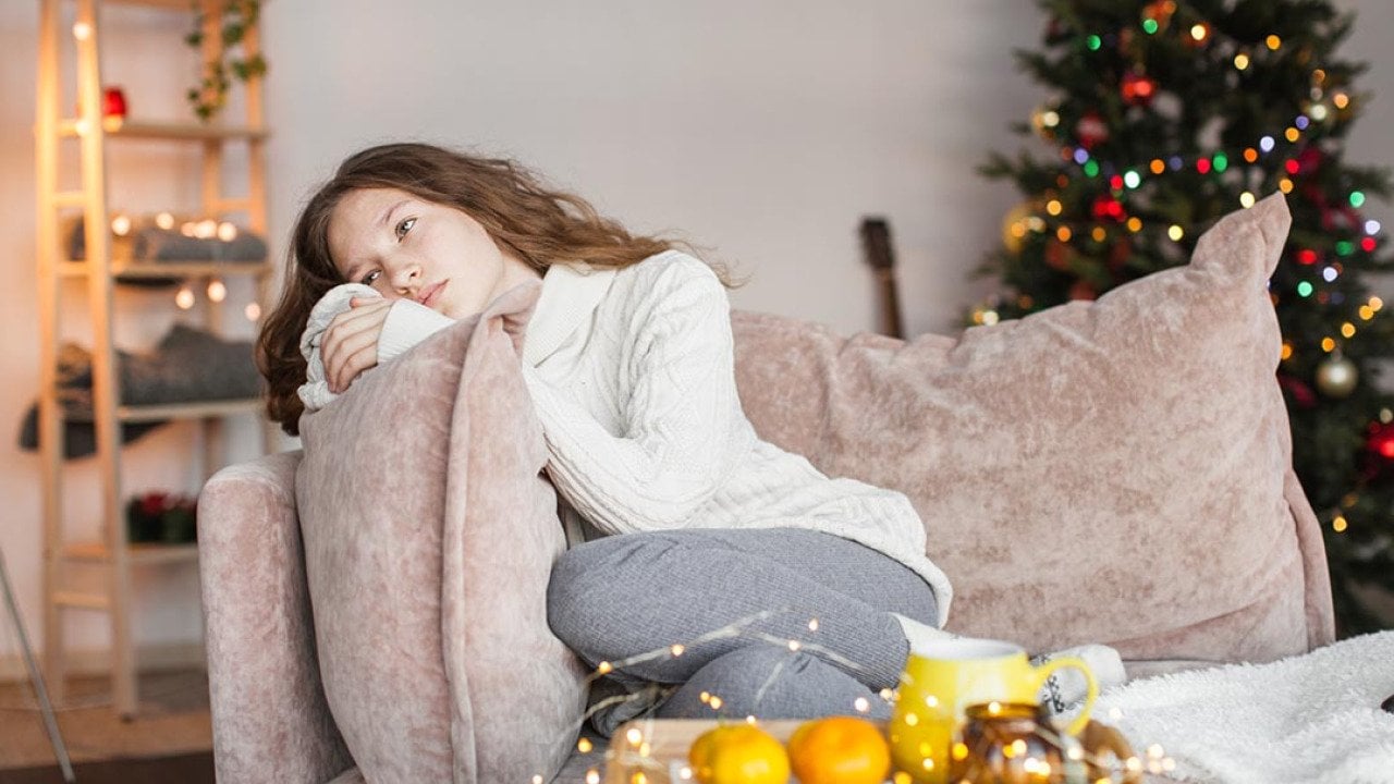 A sad young woman sitting on a sofa during the holidays.