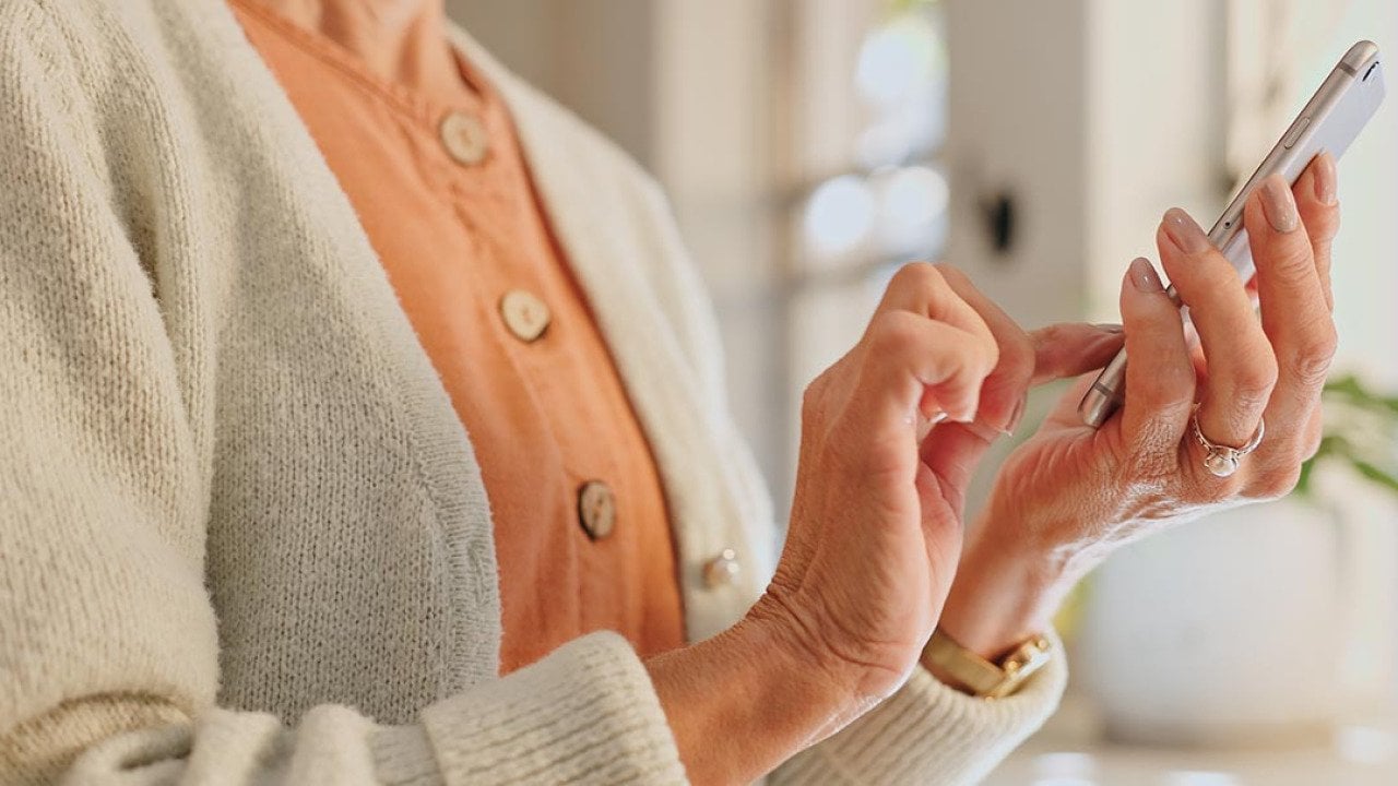 Older woman wearing a peach sweater texting on her phone