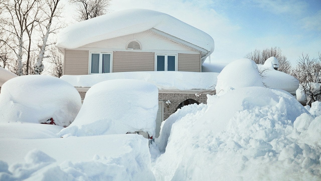 A house and its cars covered in deep white snow after a blizzard.