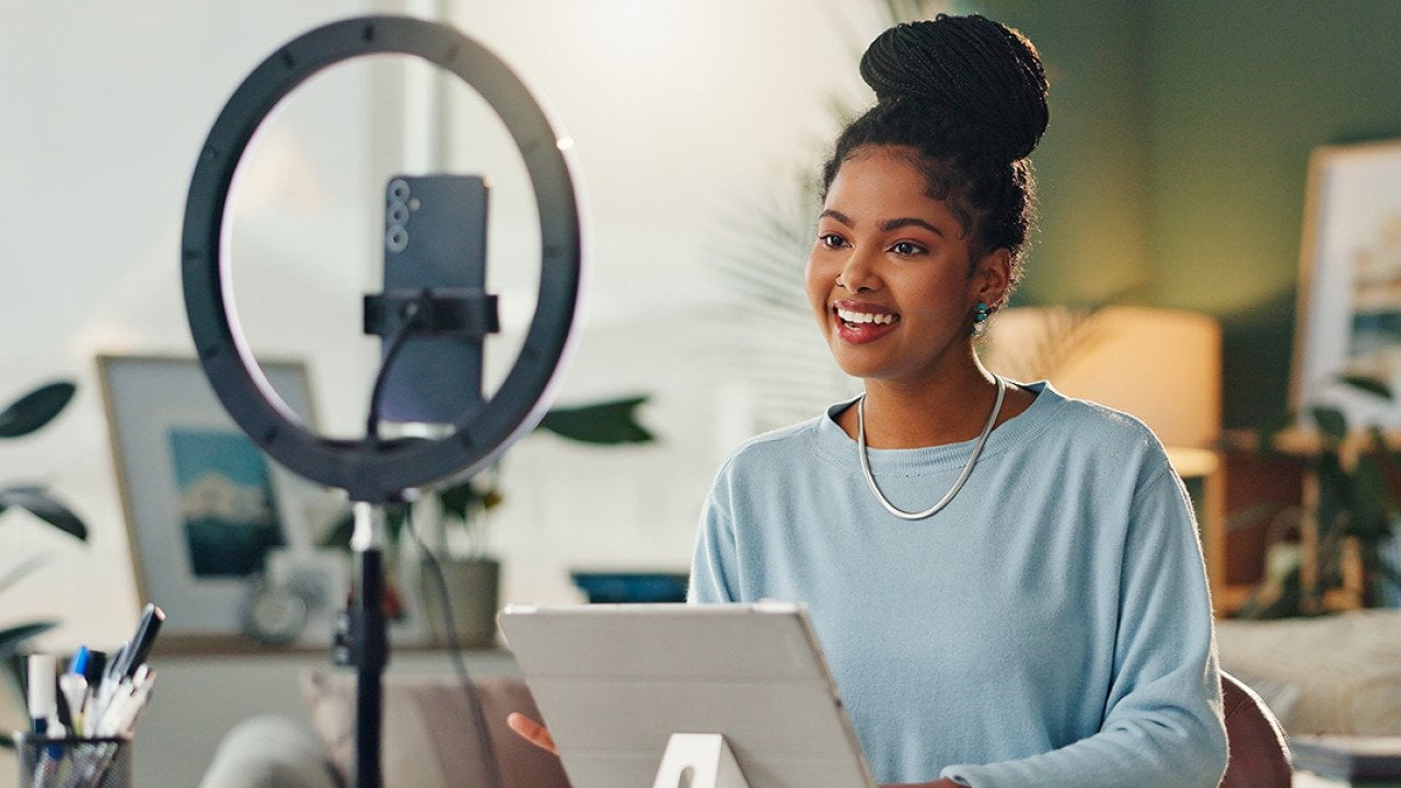 A young woman filming vlog content at home using her smartphone and a tripod.