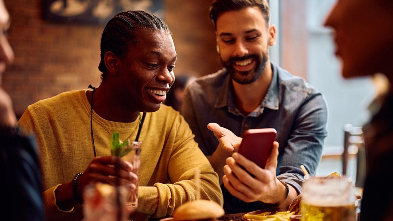 Happy men looking on their phones while sitting in a bar.