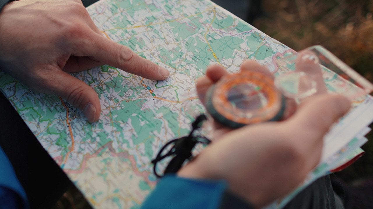 Close up on a traveler's hands navigating a trail map and compass.