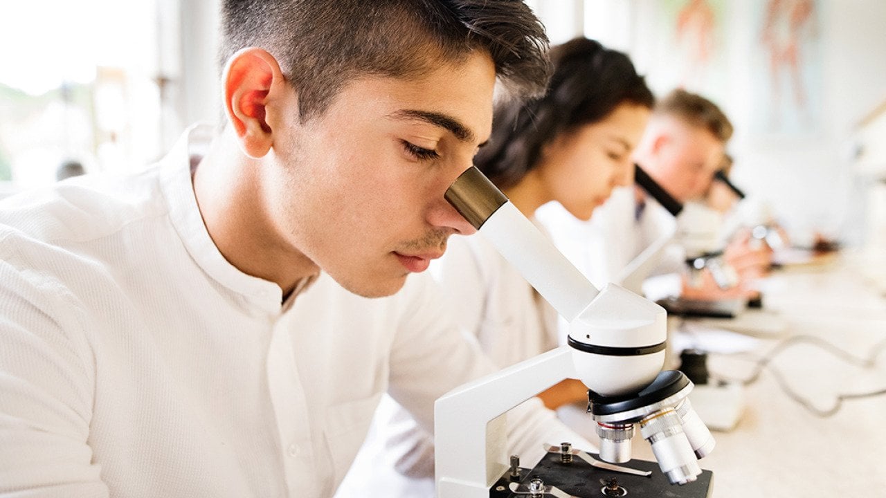 High school students working with microscopes in a laboratory.