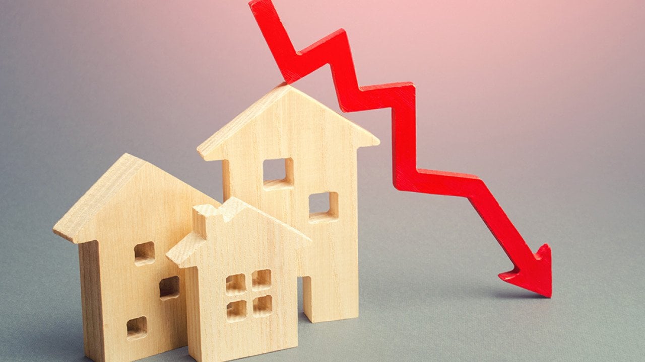 Figures of wooden homes and a red declining arrow as a concept of decline in real estate.