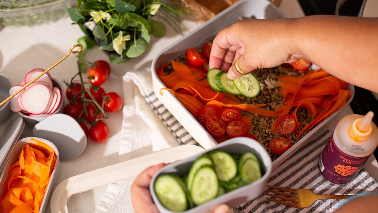 Vegetables being added on top of a healthy meal prep dish.