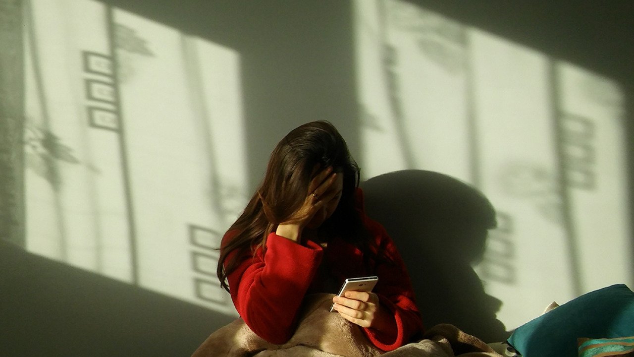 A sad woman in bed making a call on her phone.