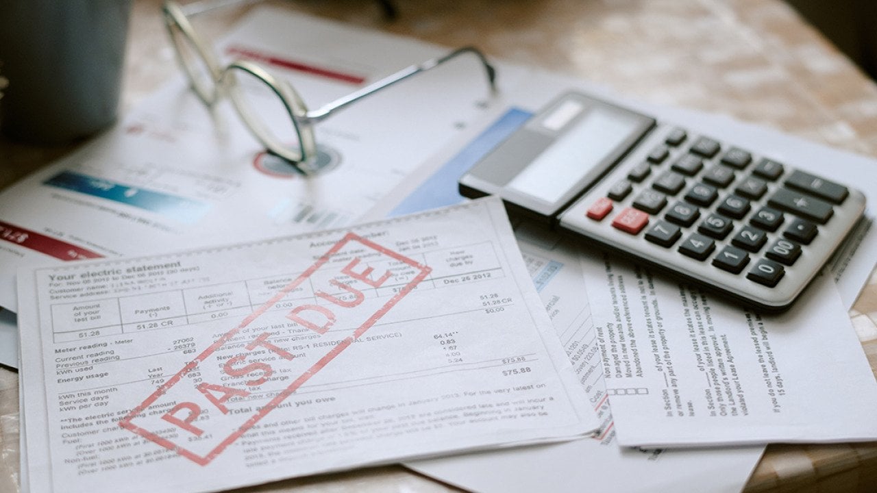 Bills stamped with a past due sign beside a calculator on top of a desk.