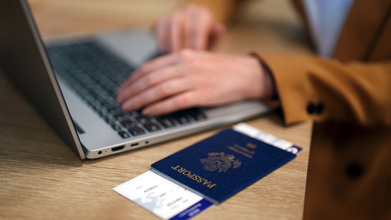 Female traveler using laptop with passport ready at the side while waiting for her flight.