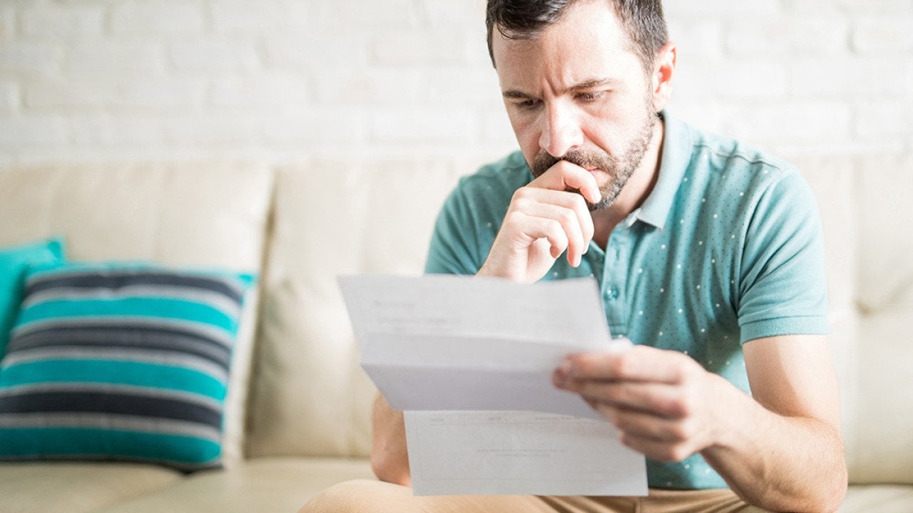 A man at home pensively looking at a debt document.