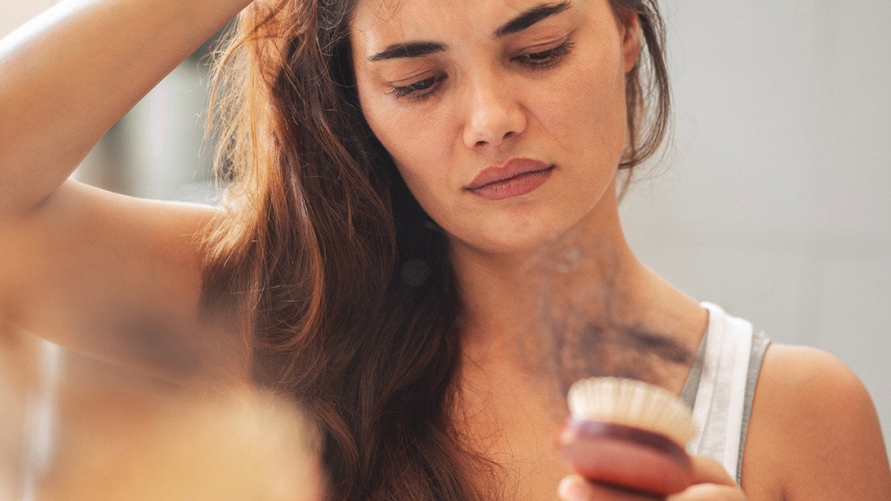 A woman staring at hair loss accumulated in her hairbrush.