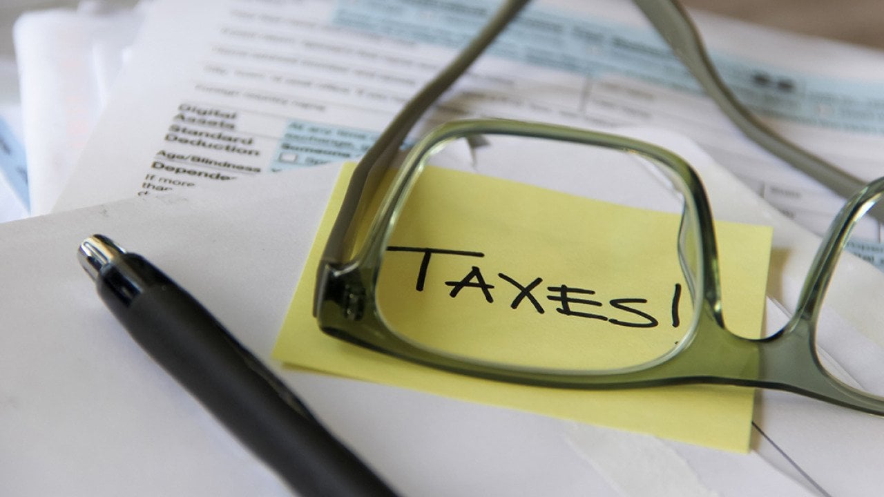 A low-angle view of tax documents and the word 'Taxes' written on a yellow sticky note viewed through eyeglasses.