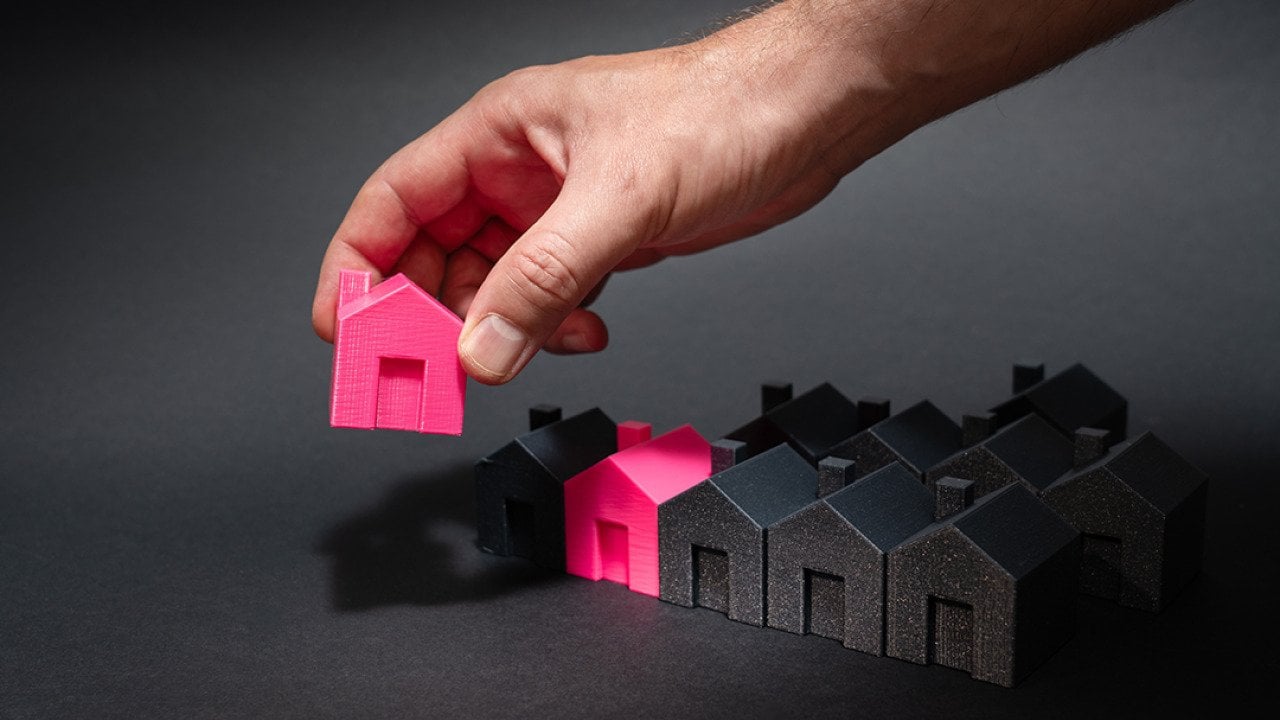 Figures of pink model houses being lined up with a row of black houses as a concept of national housing supply.