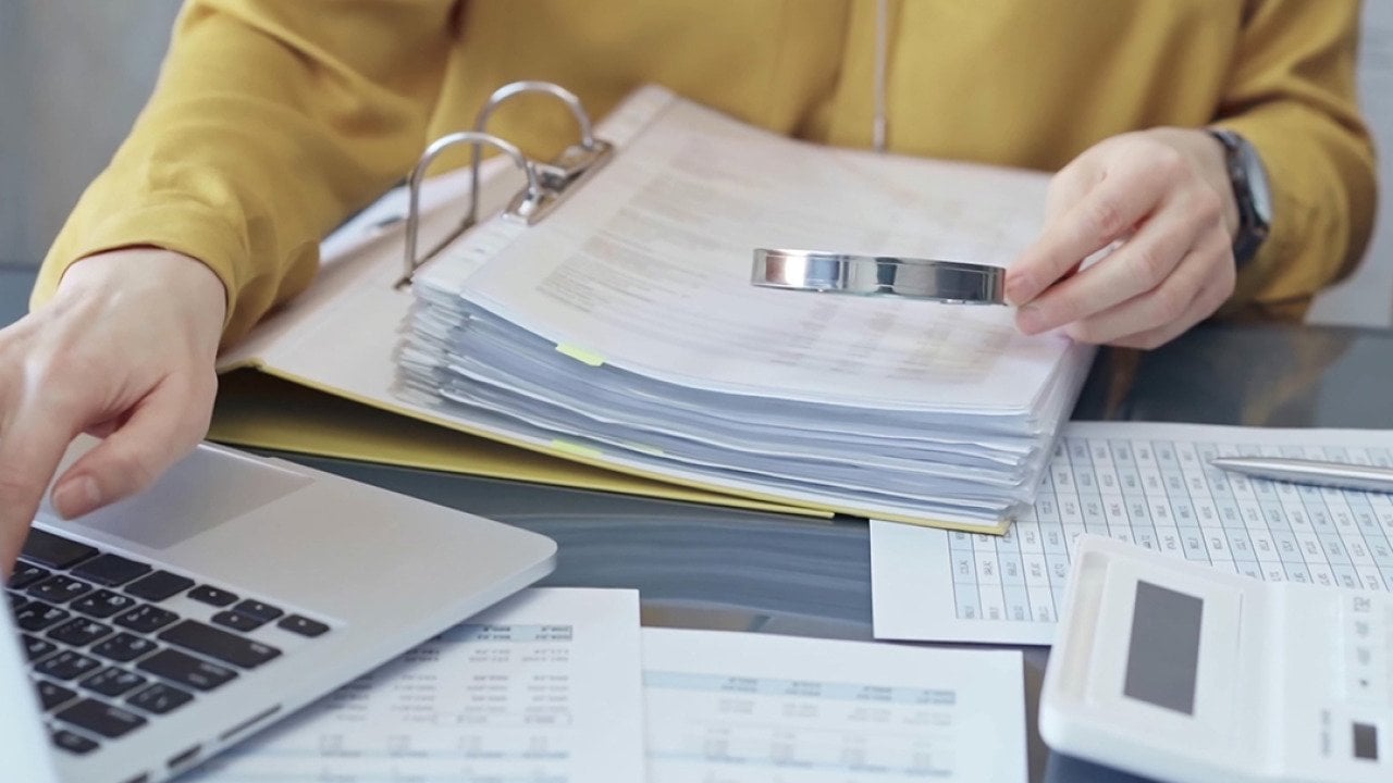 An auditor reviewing financial reports using a magnifying glass.