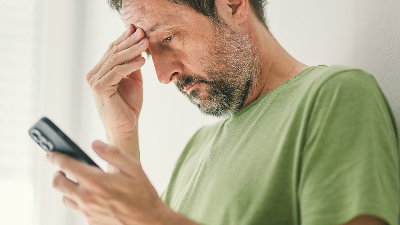 Man at home reading a worrying text message.