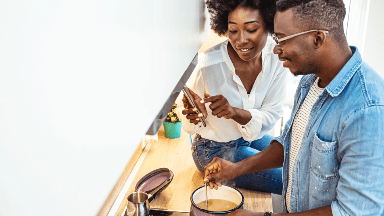 Young couple is using a smartphone and smiling while cooking in kitchen at home.