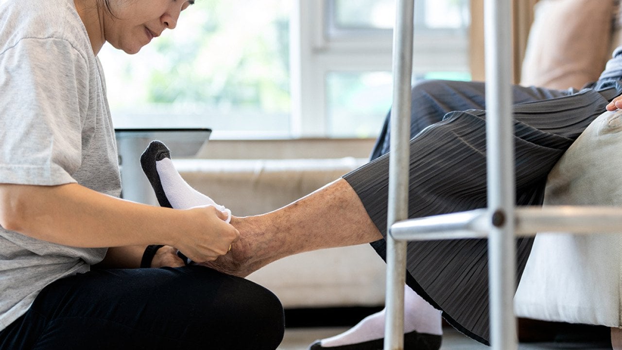 A female caregiver helping a senior person to wear socks at home.