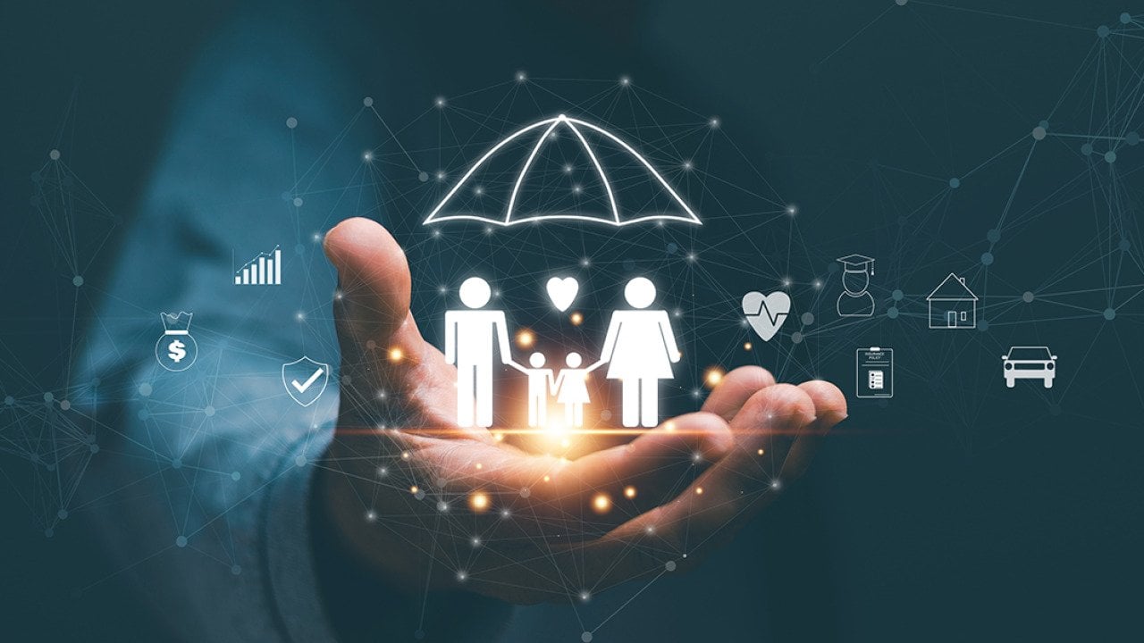 Person's hand holding hologram graphics of a family with an umbrella as a concept of life insurance.