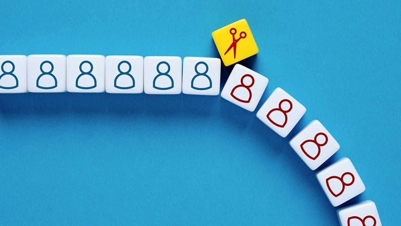 A scissor symbol on a block cutting through a row of human figures as a concept of mass layoffs.