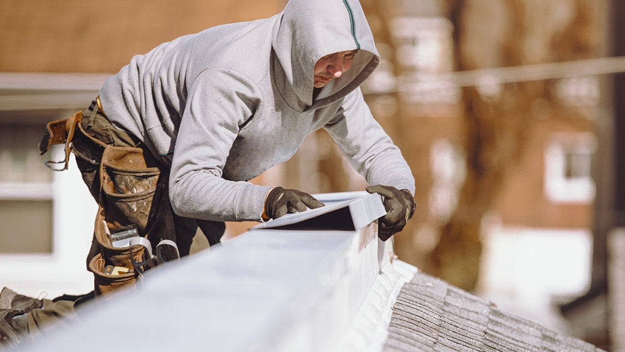 A repairman putting a metal ridge on top of a roof.